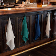 Sir|Madam Linen Frayed Edge Napkins in Dove, displayed on a wooden bar, highlighting their practical design with frayed edges and hand-sewn buttonholes.