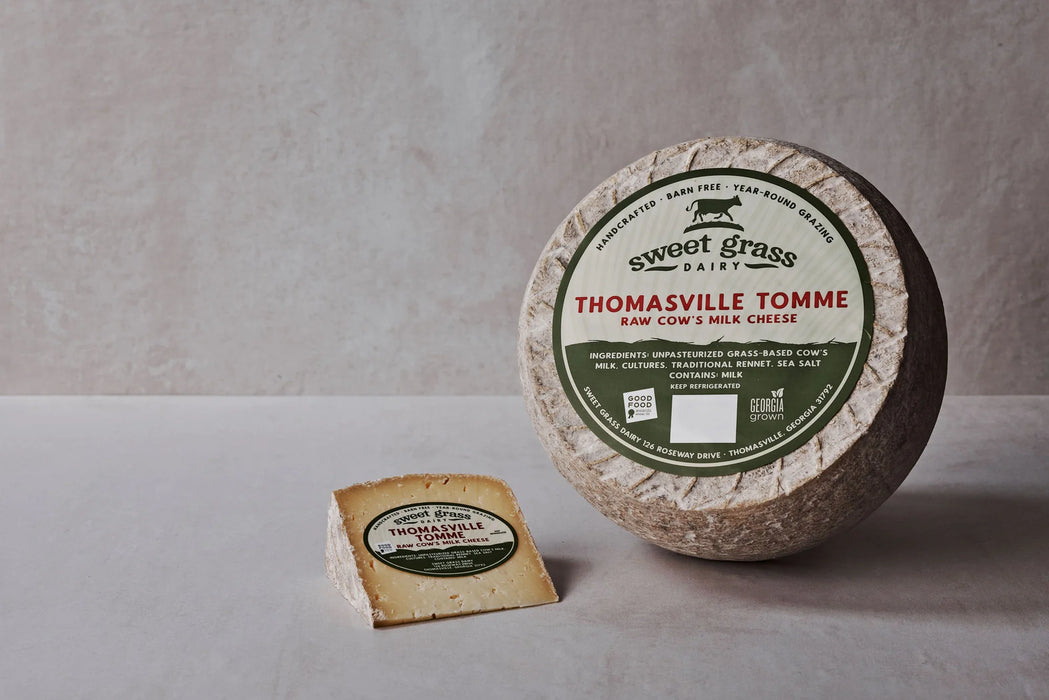 Sweet Grass Dairy | Thomasville Tomme cheese wheel with a slice cut, showcasing its natural rind and semi-soft texture.