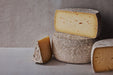 Sweet Grass Dairy | Thomasville Tomme: A semi-soft, natural-rinded cheese, showcased among other cheeses, highlighting its French farmhouse style and creamy texture.