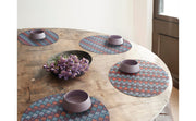 Chilewich | Kite Placemats - Gemstone - Round on a table, featuring a vibrant geometric design with a bowl of purple flowers, enhancing tableware aesthetics.