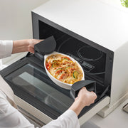 Removing a gratin-filled dish with Yamazaki Home Magnetic Pot Holders, Silicone, Black, highlighting their heat-resistant grip in a kitchen setting.
