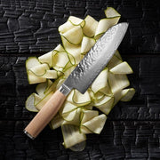 Shun | Premier Blonde Santoku, 7, with a hammered finish and light wooden handle, displayed on vegetable ribbons, showcasing its versatile cutting capabilities.