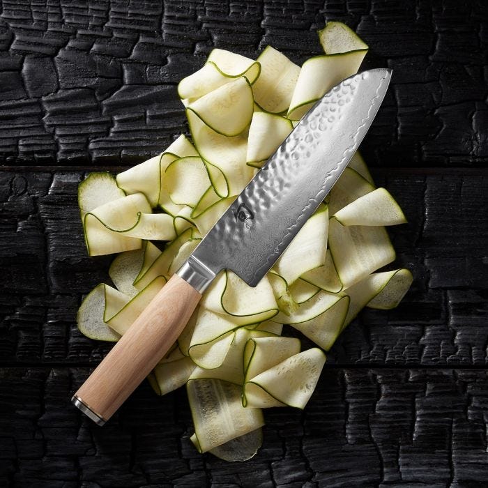 Shun | Premier Blonde Santoku, 7, with a hammered finish and light wooden handle, displayed on vegetable ribbons, showcasing its versatile cutting capabilities.