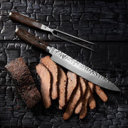 Shun Premier Carving Set Walnut, 2-Piece, featuring a sliced, pepper-crusted roast with a hammered-finish slicing knife and two-pronged fork on a charred-wood surface.