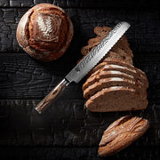 Shun Premier Bread Knife with hammered blade and walnut handle rests on sliced artisan-style bread, showcasing its precise cutting through the loaf's crusty texture.