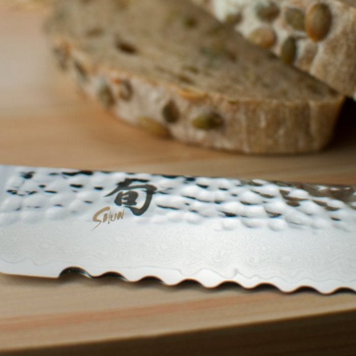 Shun Premier Bread Walnut, 9 knife with serrated blade and Damascus pattern on a cutting board, ideal for slicing whole-grain bread without crushing or tearing.
