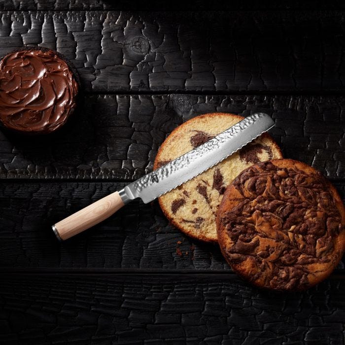 Shun Premier Blonde Bread Knife slicing a marbled cake, showcasing its precise serrations and elegant design, with chocolate spread nearby for added indulgence.