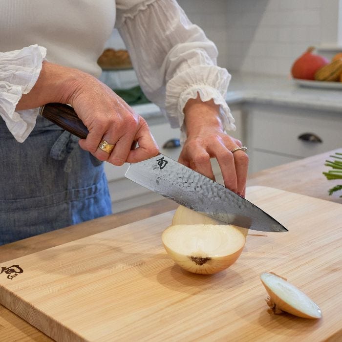 Slicing onion with Shun | Premier Chef's Walnut, 8 inches knife, showcasing hammered finish and logo, highlighting its precision and craftsmanship in a home kitchen setting.