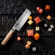 Shun Premier Blonde Nakiri, 5.5, with a hammered Damascus finish, rests on a blackened surface, surrounded by neatly cubed fruits.