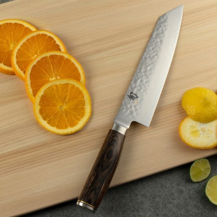 Shun Premier Kiritsuke Walnut, 8, on a wooden board with orange slices, halved lemon, and lime wedges, showcasing its versatility for slicing and precision cutting.