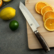 Shun Premier Kiritsuke Walnut, 8, knife on a cutting board with sliced oranges, showcasing its precision and versatility for kitchen tasks.
