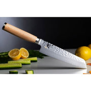 Shun Premier Blonde Master Utility knife with a hammered blade and light wood handle on a cutting board, surrounded by lemon halves, cucumber batons, and carrot slices.