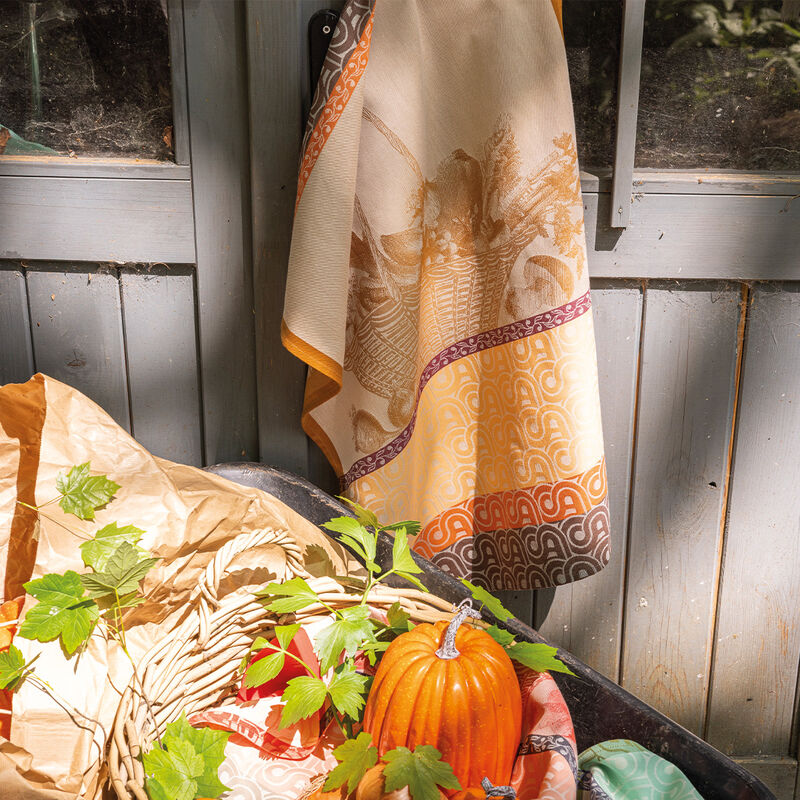 Le Jacquard Français Potager D'Hiver Tea Towel in a rustic setting with seasonal décor, featuring an orange pumpkin and leafy vines in a black trough.