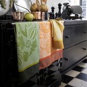 Le Jacquard Francais Thanksgiving Tea Towel, Green, displayed on a glossy black range, alongside kitchen tools, enhancing the cozy, curated kitchen ambiance of Athens Cooks.