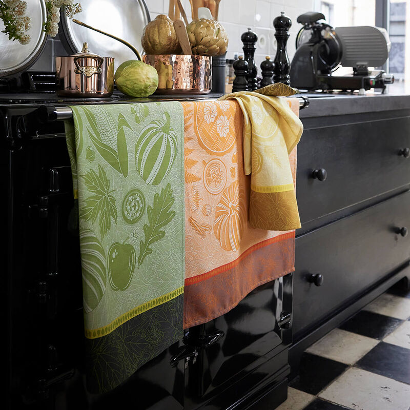 Le Jacquard Francais Thanksgiving Tea Towel, Green, displayed on a glossy black range, alongside kitchen tools, enhancing the cozy, curated kitchen ambiance of Athens Cooks.