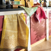 Le Jacquard Français | Vignoble Tea Towel, Yellow, draped on red cabinets in a cozy kitchen, featuring vineyard design, with cutting board and teapot on the countertop.
