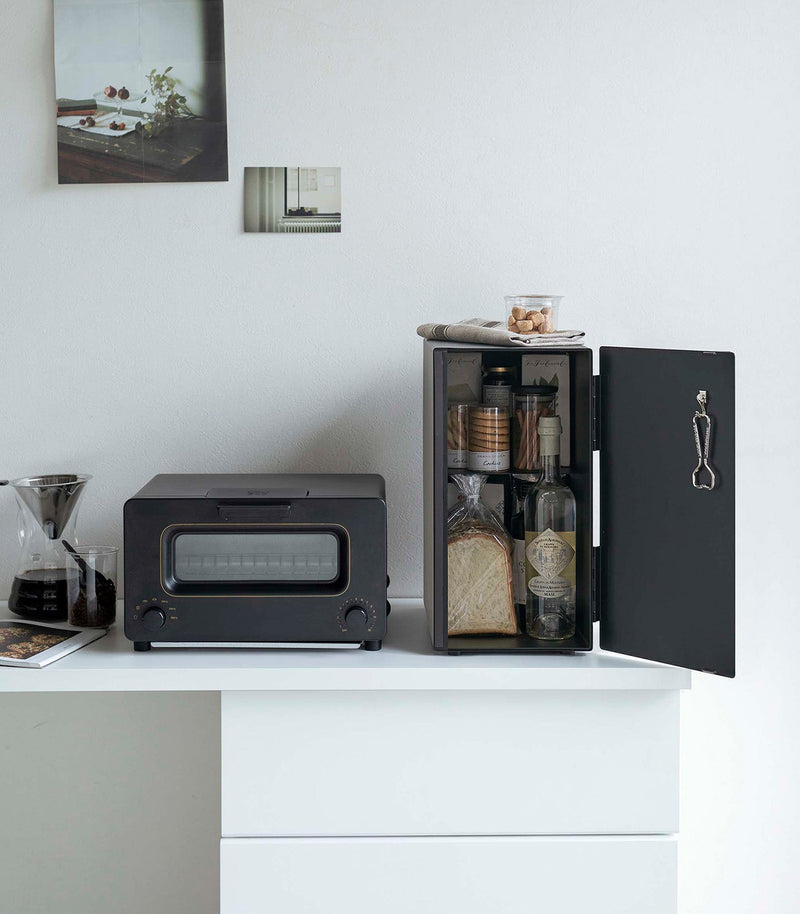 Yamazaki Home Bread Box in black steel on a minimalist countertop, keeping baked goods organized and fresh, with a nearby pour-over coffee setup and mini-oven.