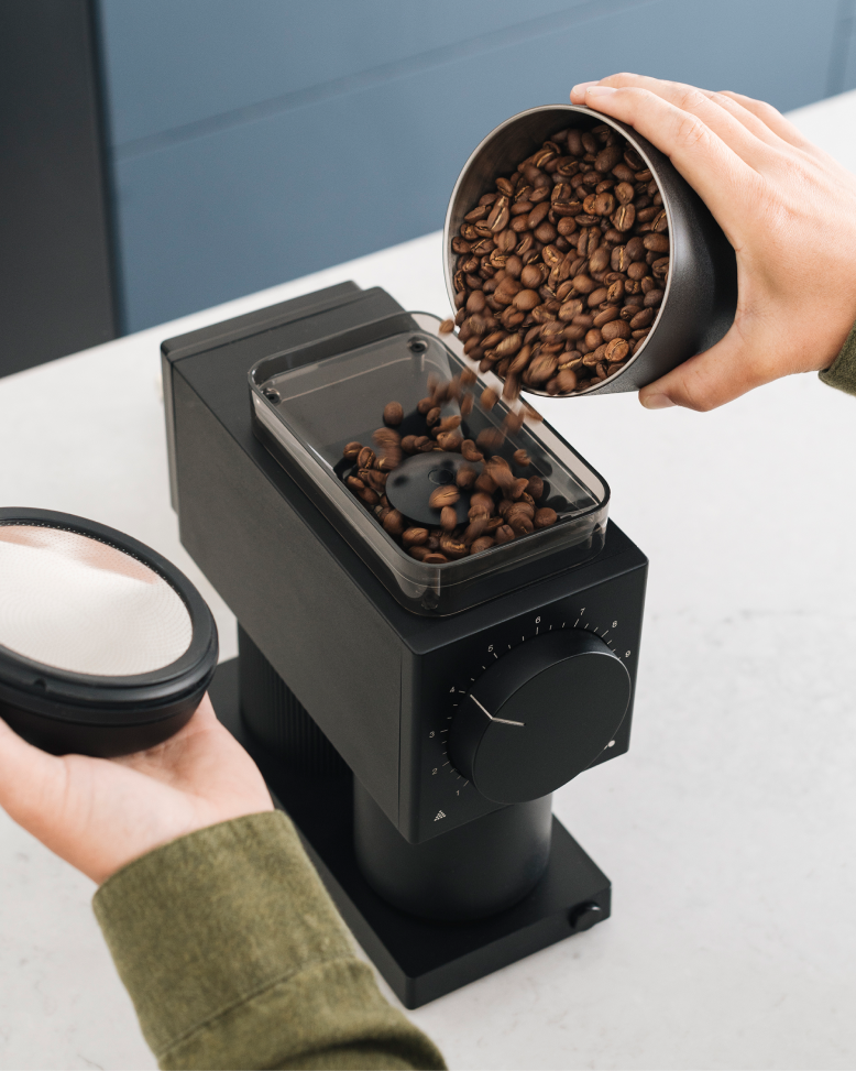 FELLOW | Ode Brew Grinder Gen 2, Matte Black: Pouring beans into the grinder's hopper, showcasing its professional-grade flat burrs and mesh filter for precise coffee brewing.