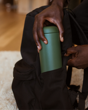 FELLOW | Carter Move Mug, Cargo Green, 16 oz, being slipped into a backpack's side pocket, highlighting its portability and spill-proof design for convenient travel use.