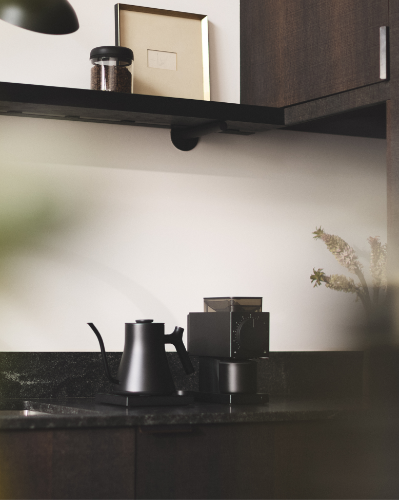 Fellow | Stagg EKG Pro Electric Kettle, Matte Black with Walnut Accents, on a modern countertop beside a matching coffee grinder, ideal for precise coffee brewing.