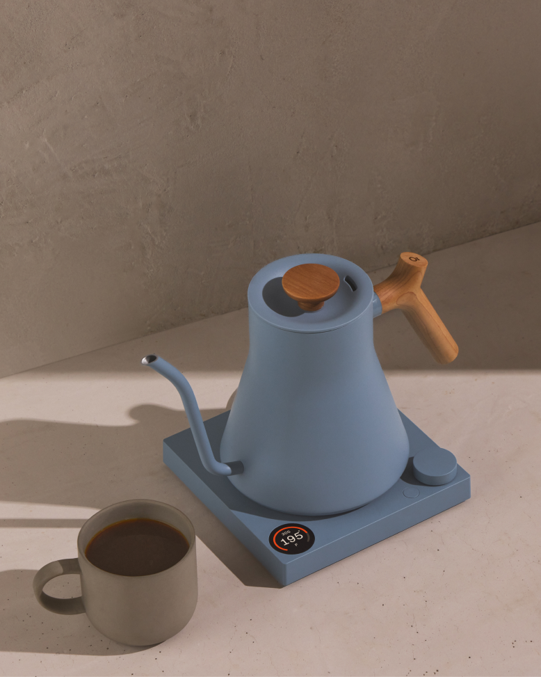FELLOW | Stagg EKG Pro Electric Kettle in Hazy Blue with Maple handle on a countertop, showcasing precise temperature control for perfect pour-over coffee.