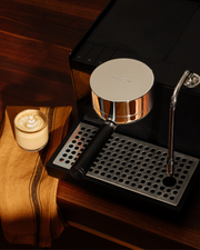 FELLOW | Espresso Series 1, Black machine with portafilter and steam wand, beside a latte with heart art on a kitchen towel, showcasing professional home espresso setup.