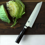 Shun Dual Core Kiritsuke knife with Damascus-pattern blade and octagonal handle on a wooden board, beside sliced savoy cabbage, embodying expert craftsmanship and culinary precision.