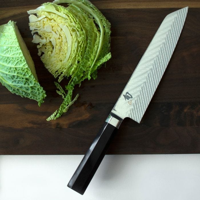 Shun Dual Core Kiritsuke knife with Damascus-pattern blade and octagonal handle on a wooden board, beside sliced savoy cabbage, embodying expert craftsmanship and culinary precision.