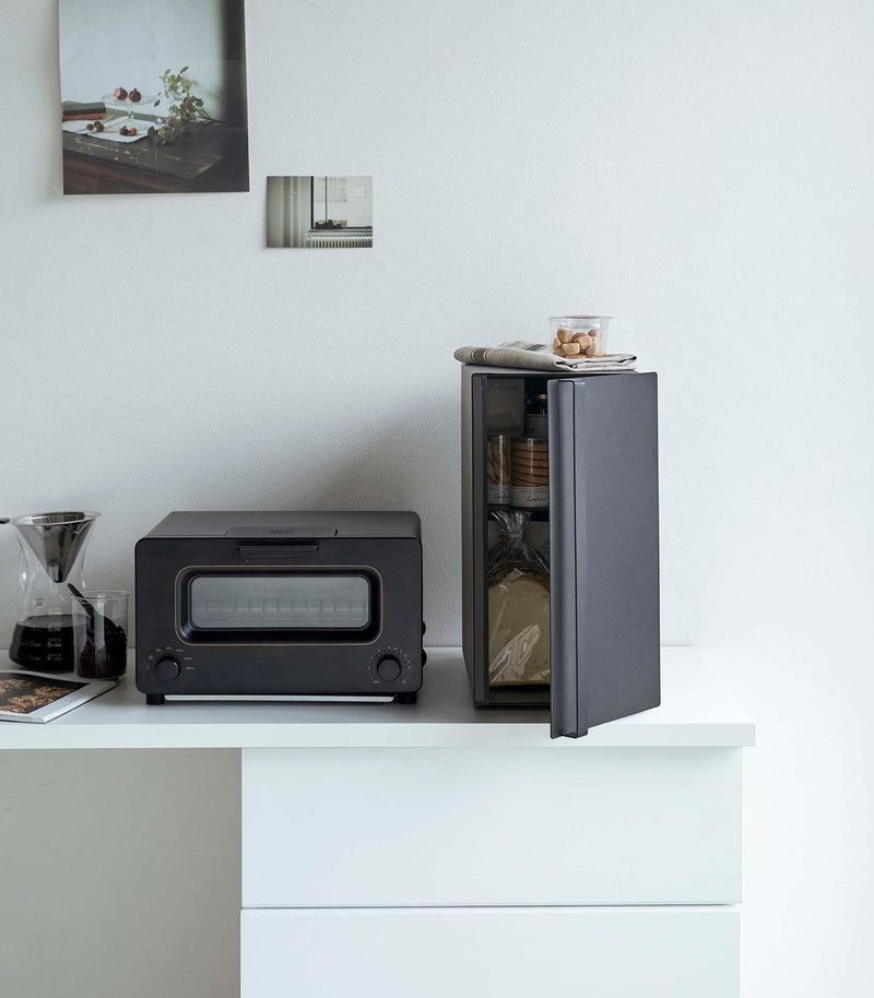 Yamazaki Home | Bread Box, Vertical, Steel, Black, keeping baked goods fresh, sits open revealing cookie jars, enhancing kitchen decor alongside a toaster-oven and coffee dripper.