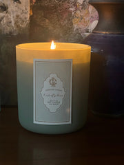 Lodestone Candles | Violet & Moss Candle with a lit flame and labeled jar, displayed on a table, showcasing its elegant design.