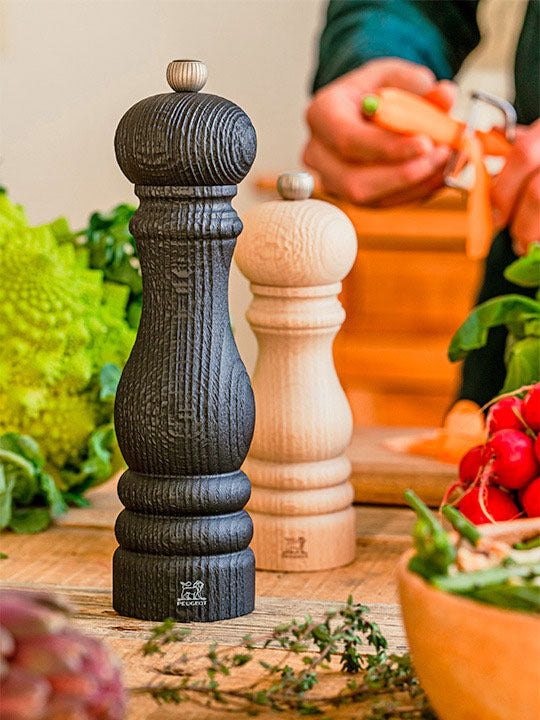 Peugeot | Paris Nature Collection Pepper Mill, Nature Black on a rustic countertop with fresh vegetables, highlighting its eco-friendly design and durable mechanism, perfect for culinary enthusiasts.
