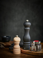 Peugeot | Paris Nature Collection Pepper Mill, Nature Black, shown with oak spice mill and glass jar of peppercorns, illustrating eco-friendly design and adjustable grind.