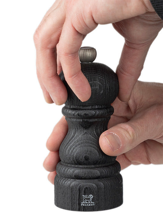 Hands twist the top of a Peugeot | Paris Nature Collection Pepper Mill, Nature Black, showcasing its eco-friendly design and adjustable metal grind setting.