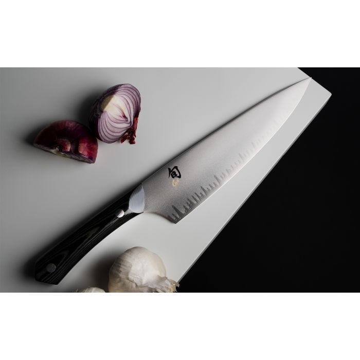 Shun | Narukami 8 Chef's Knife on cutting board with halved red onion and garlic, showcasing its polished blade with Japanese characters and black handle.