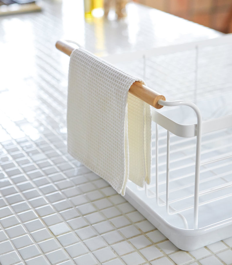 Yamazaki Home | Steel + Wood Dish Rack with Drainer Spout on a minimalist kitchen counter, featuring a wooden dowel with waffle-weave towels.