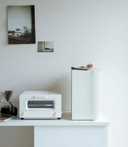 Yamazaki Home | Bread Box, Vertical, Steel, Black on counter, enhancing minimalist kitchen decor with a folded towel and cookies jar on top.