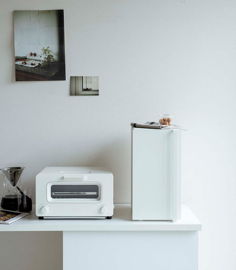 Yamazaki Home | Bread Box, Vertical, Steel, Black on counter, enhancing minimalist kitchen decor with a folded towel and cookies jar on top.