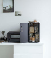 Yamazaki Home | Bread Box, Vertical, Steel, Black neatly stores bread and snacks beside a tidy kitchen setup with a toaster-oven and pour-over coffee setup.