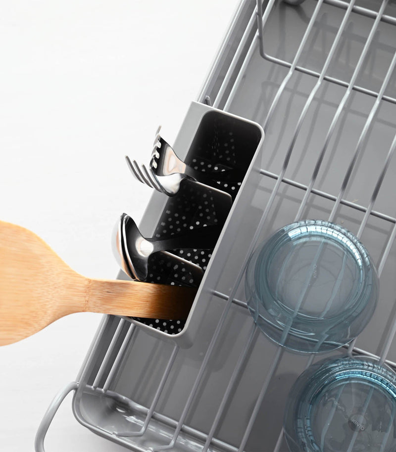 Yamazaki Home | Steel + Wood Dish Rack with Drainer Spout featuring steel frame, wooden handles, and utensil holder, displayed with a dishwasher's cutlery and bowls.