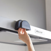Hand pulling down a black magnetic pot holder from a kitchen range hood, showcasing the Yamazaki Home Silicone Pot Holders, ideal for safe handling in the kitchen.