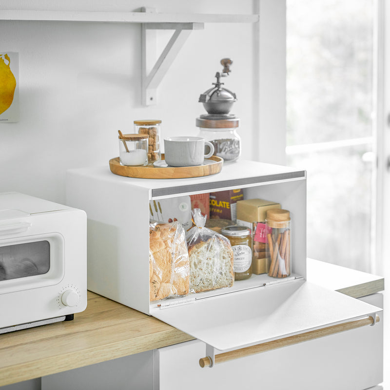 Yamazaki Home's Simple Steel Bread Box in White + Wood stylishly organizes bread and snacks on a minimalist kitchen countertop, offering a clutter-free storage solution.