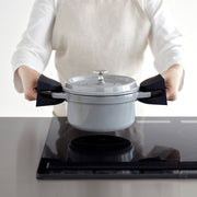 Person uses Yamazaki Home Magnetic Pot Holders, Silicone, Black, to safely lift a lidded grey pot from an induction cooktop.