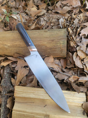 Rhymer Knives | 8 Chef Knife featuring African Blackwood and Rams Horn with Copper Bolster, displayed on a log, emphasizing its hand-forged craftsmanship and superior handling.
