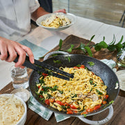 Staub Perfect Pan 14.5-inch Matte Black wok with wide sides and a glass lid, ideal for diverse cooking methods like stir-frying and steaming.