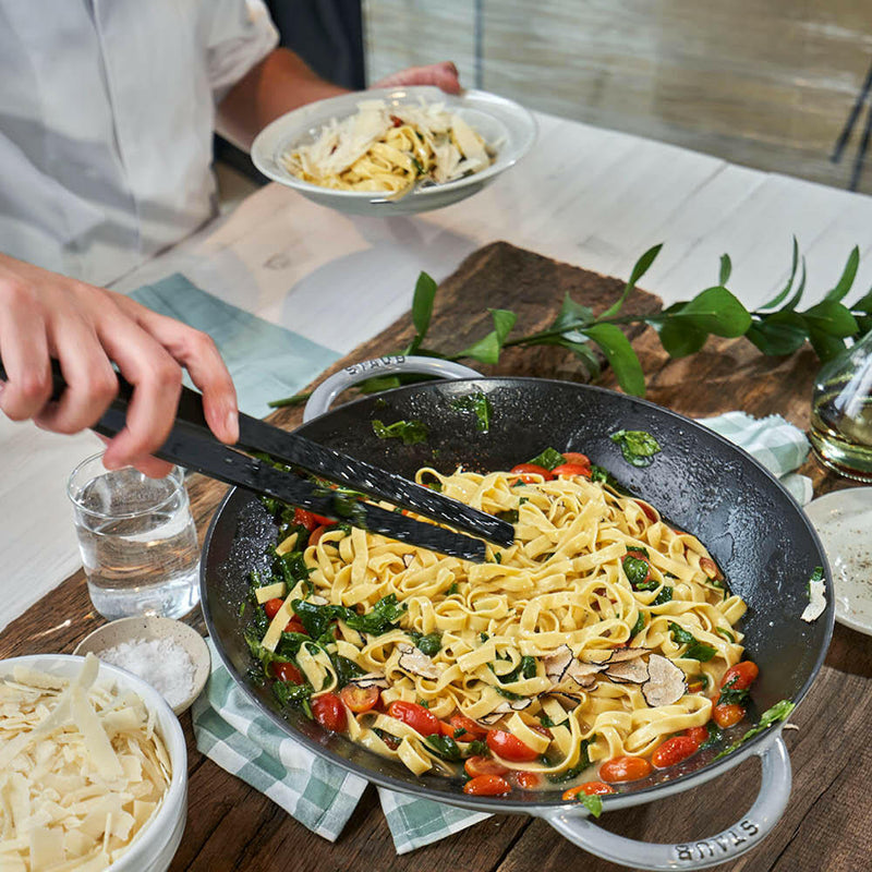 Staub Perfect Pan 14.5-inch Matte Black wok with wide sides and a glass lid, ideal for diverse cooking methods like stir-frying and steaming.