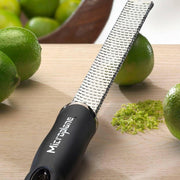 Microplane | Premium Zester, Grater - Classic Blue, shown resting on wood with limes and zest, ideal for effortless citrus zesting and grating in culinary settings.