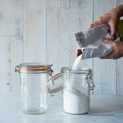 Le Parfait | Super Jars - 1L (32oz) with clamp-down lids; one jar being filled with sugar, exemplifying elegant, sustainable storage for kitchen staples.
