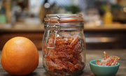 Le Parfait Rounded French Glass Storage Jar filled with sugar-coated candied citrus peels, alongside a whole citrus fruit and a small bowl of peels.