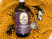 My Elderberry Fairy | Elderberry Syrup - 16 oz bottle, crafted with organic ingredients, ideal for health support, suitable for drinks, on a yellow blanket.