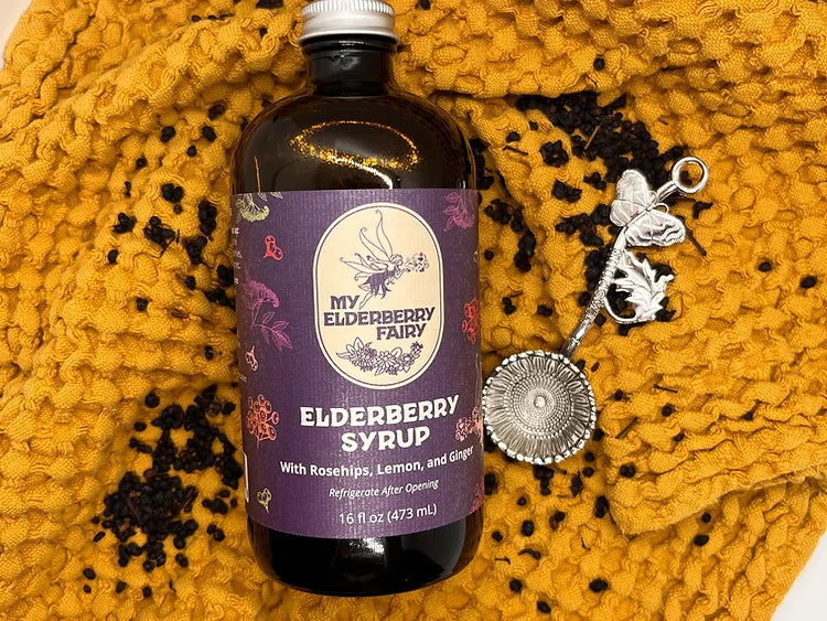 My Elderberry Fairy | Elderberry Syrup - 16 oz bottle, crafted with organic ingredients, ideal for health support, suitable for drinks, on a yellow blanket.